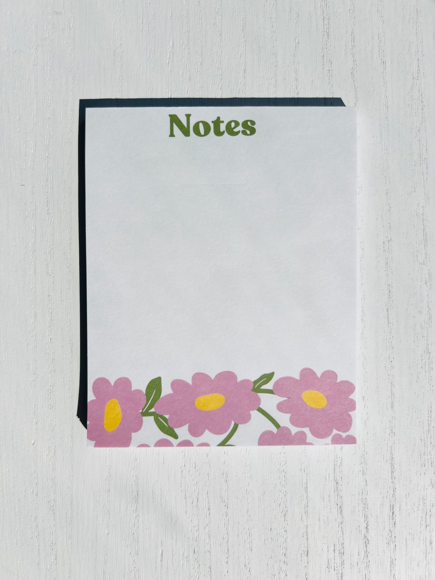 A notepad with a white cover and floral designs at the bottom, titled 'Notes' on the top.