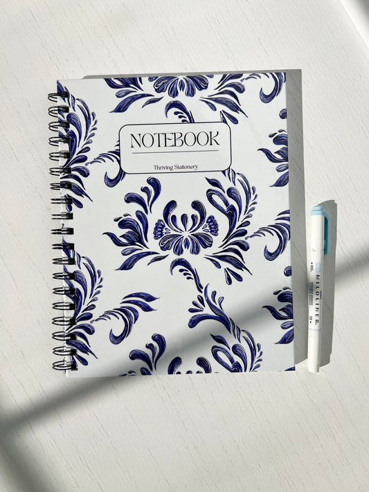 Aesthetic blue and white spiral notebook with floral design, hardcover finish, and “Notebook” label by Thriving Stationery.