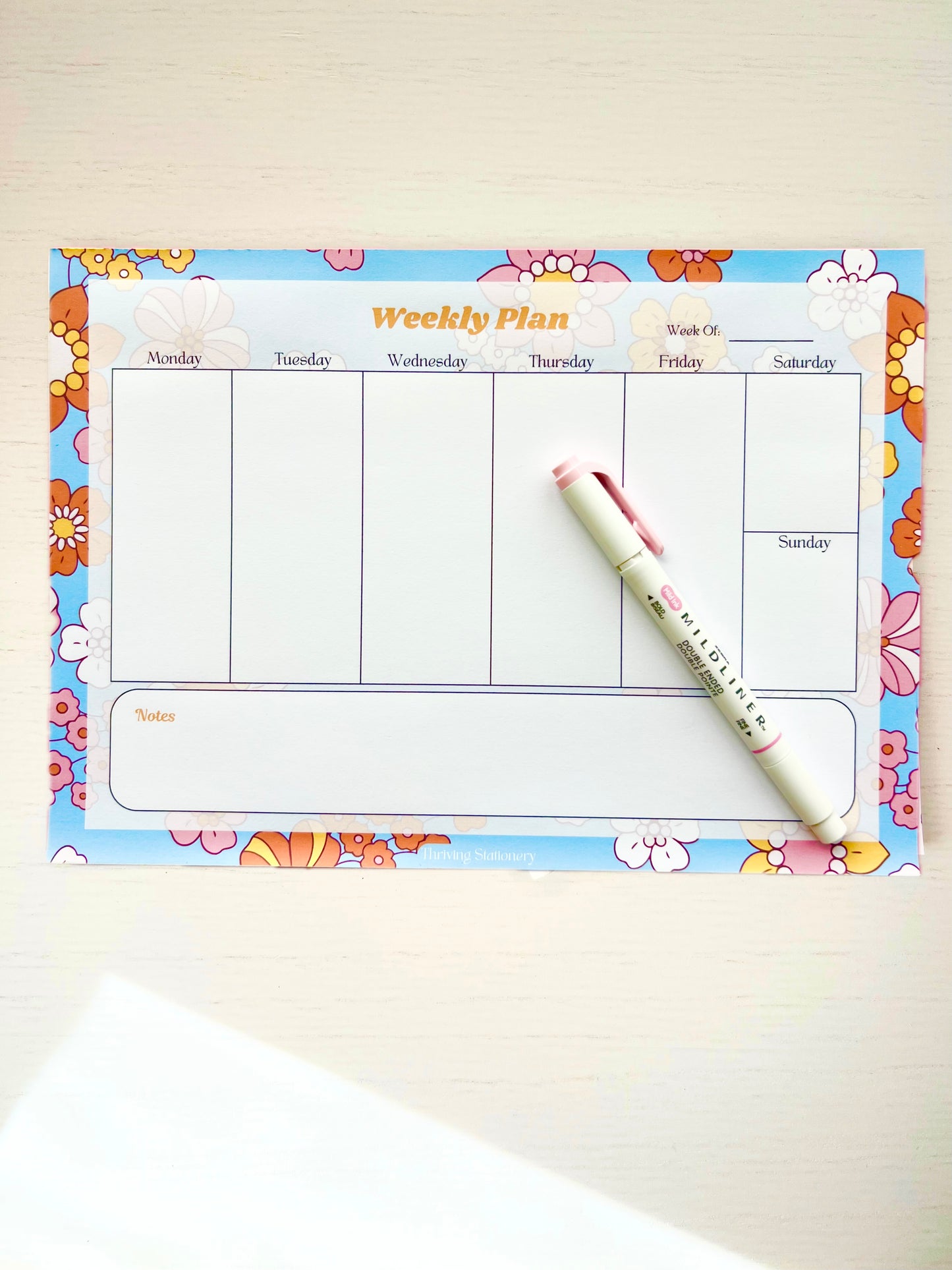 Colorful floral-themed weekly planner notepad with 7 columns for each day of the week and a large notes section at the bottom.