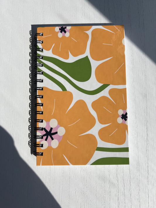 A hardcover lined journal with a floral pattern on the cover, predominantly orange and green colors, spiral bound.