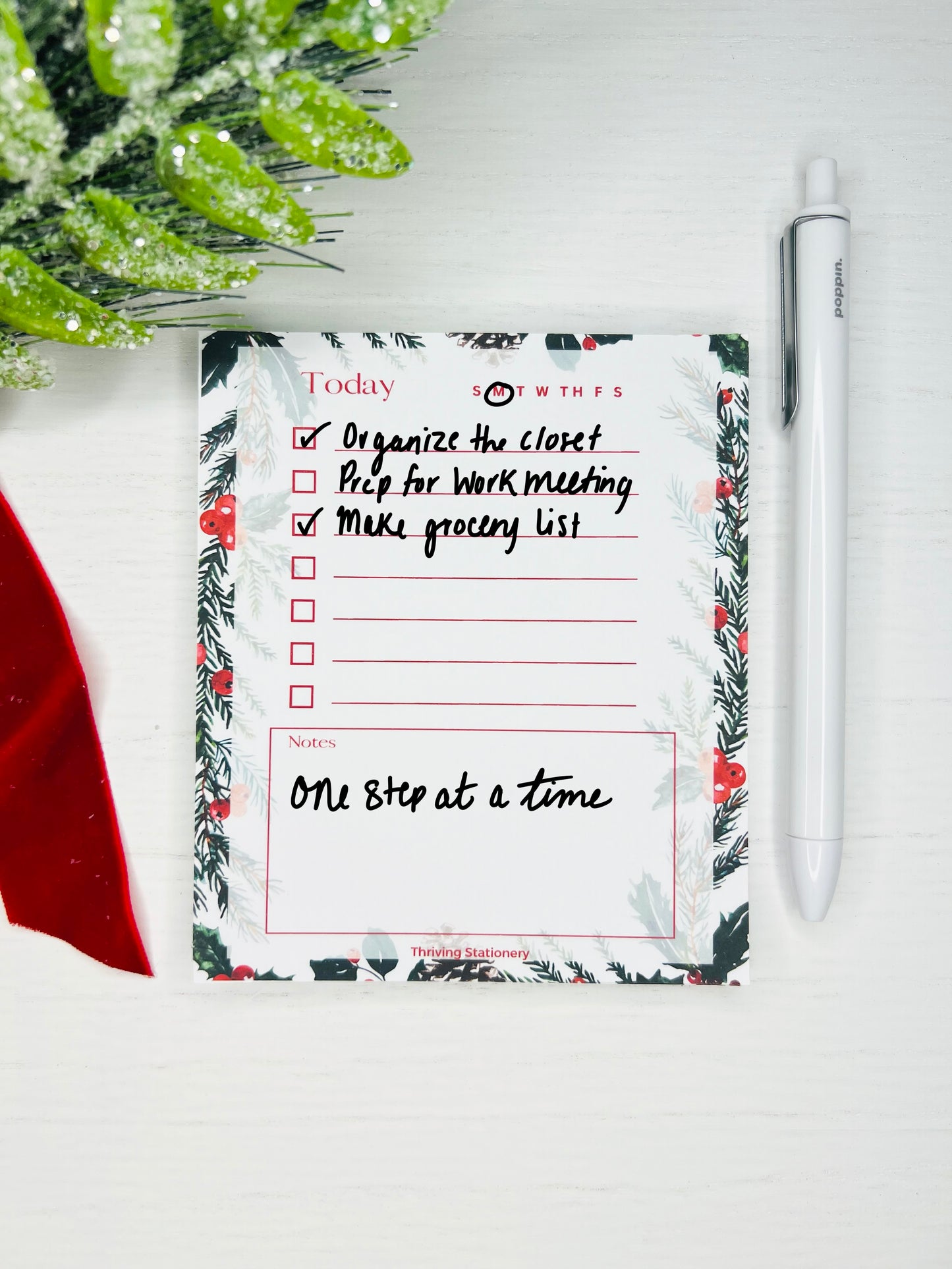 Festive daily planner notepad with pine and berry border, checkbox list section, weekday tracker, and lined notes area. Text reads “Today” with red accent lines.
