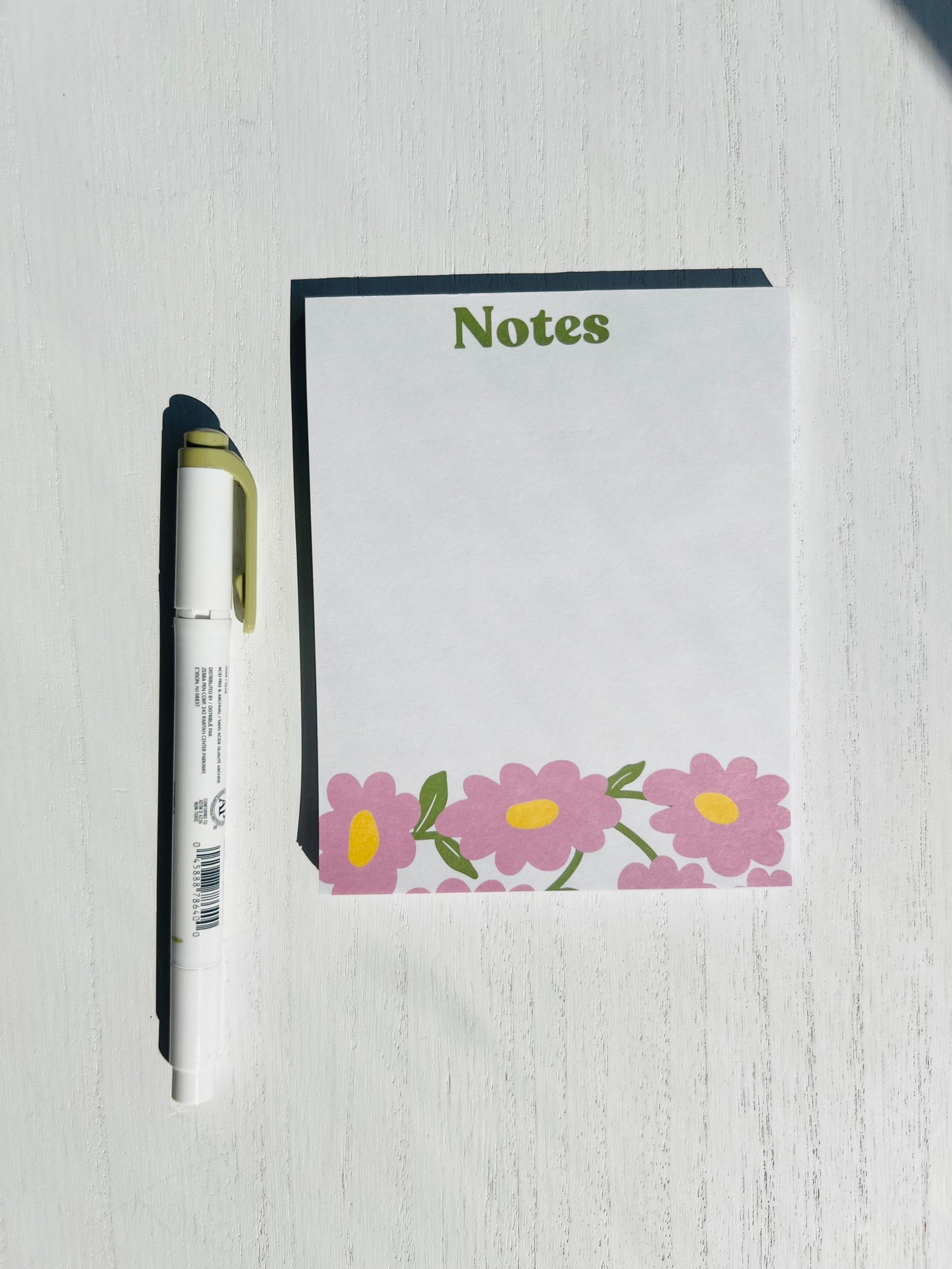 A notepad with a white cover and floral designs at the bottom, titled 'Notes' on the top.
