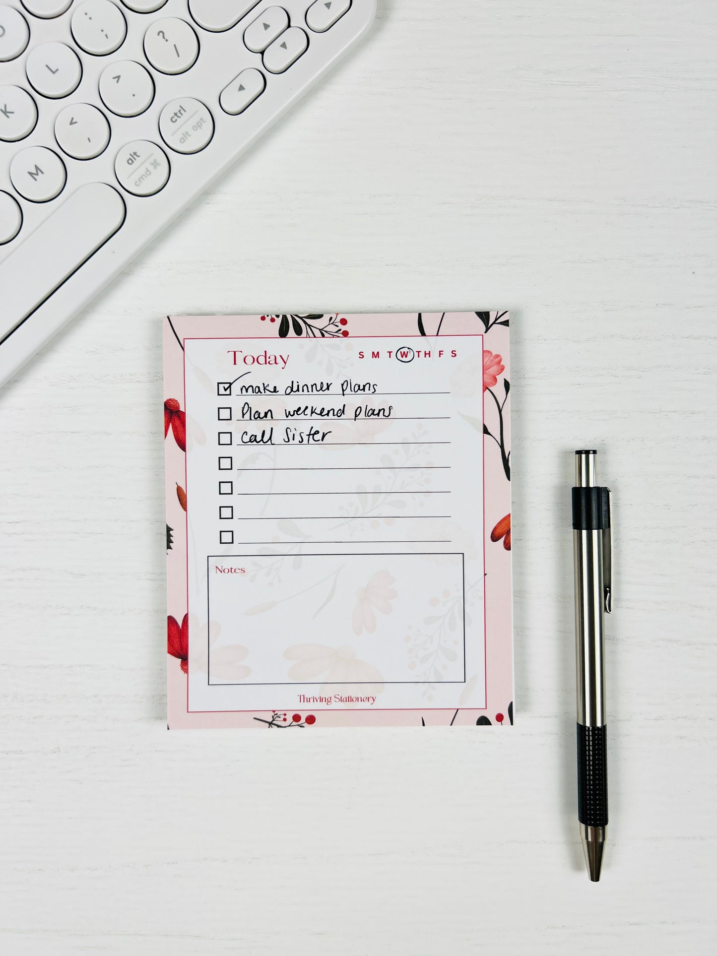 Pink Botanical Daily Planner Notepad with floral border, to-do list, and notes section with a pen and keyboard for scale