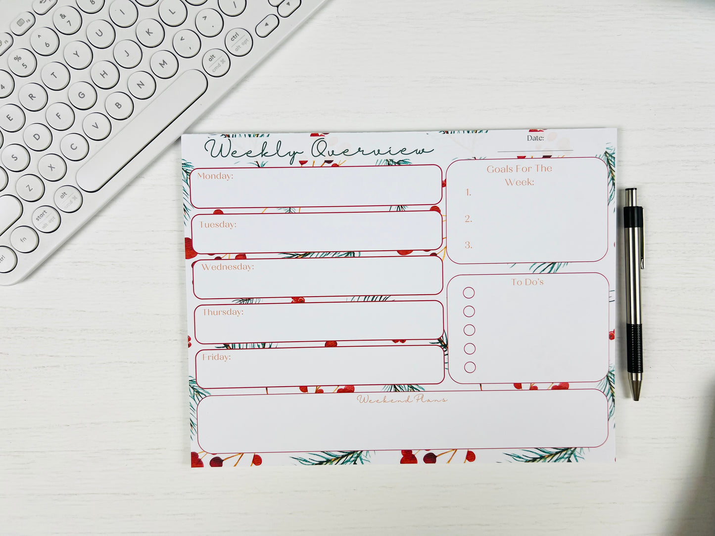 Weekly planner pad with floral design on a desk with a keyboard and pen.