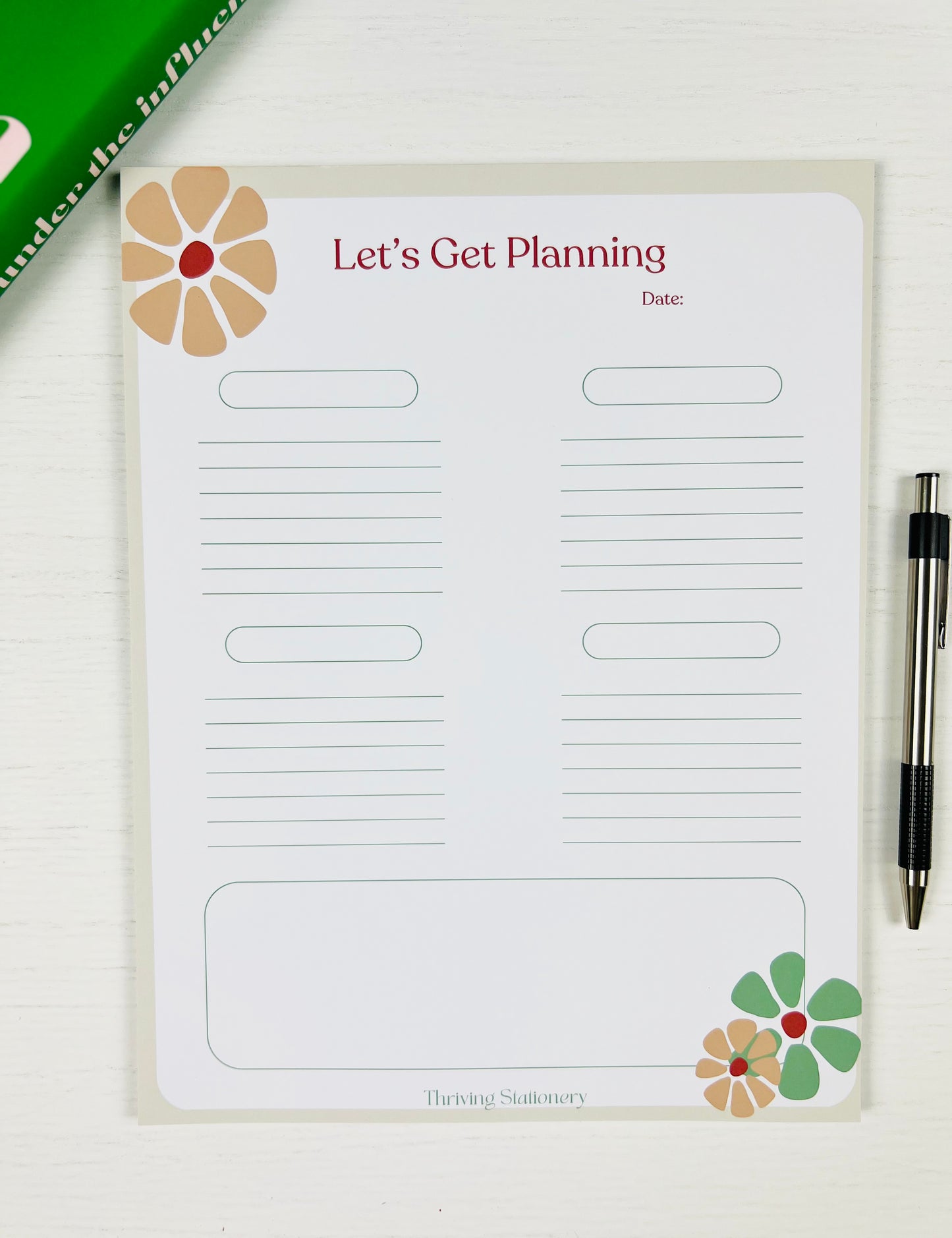 Planning pad with floral designs and text on a white surface with a pen.