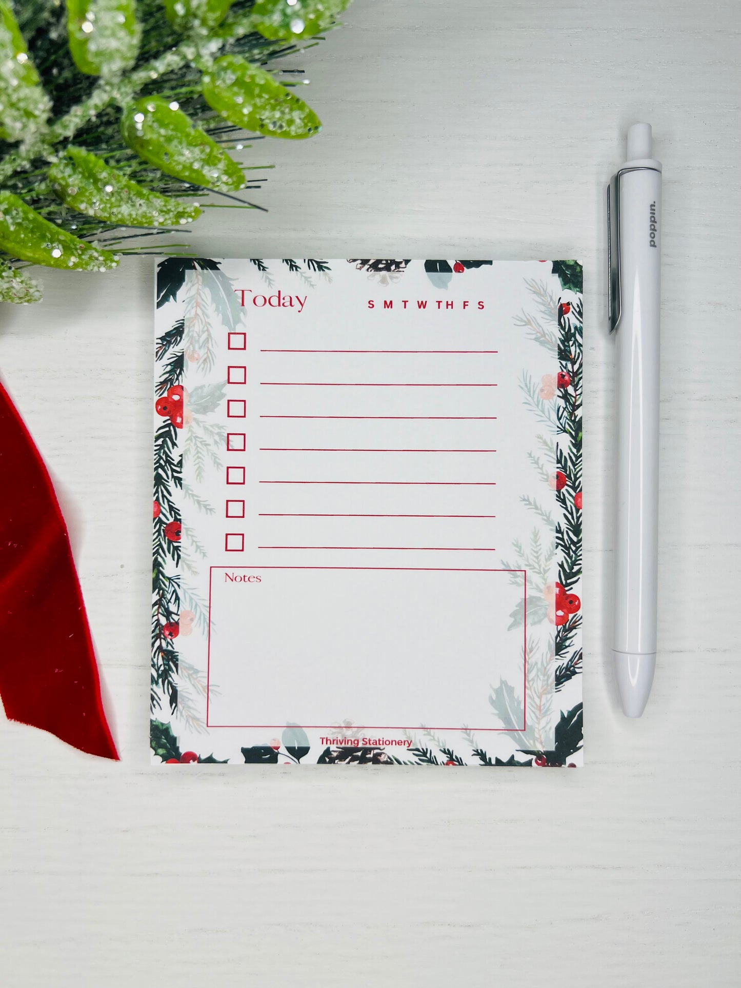 Festive daily planner notepad with pine and berry border, checkbox list section, weekday tracker, and lined notes area. Text reads “Today” with red accent lines.