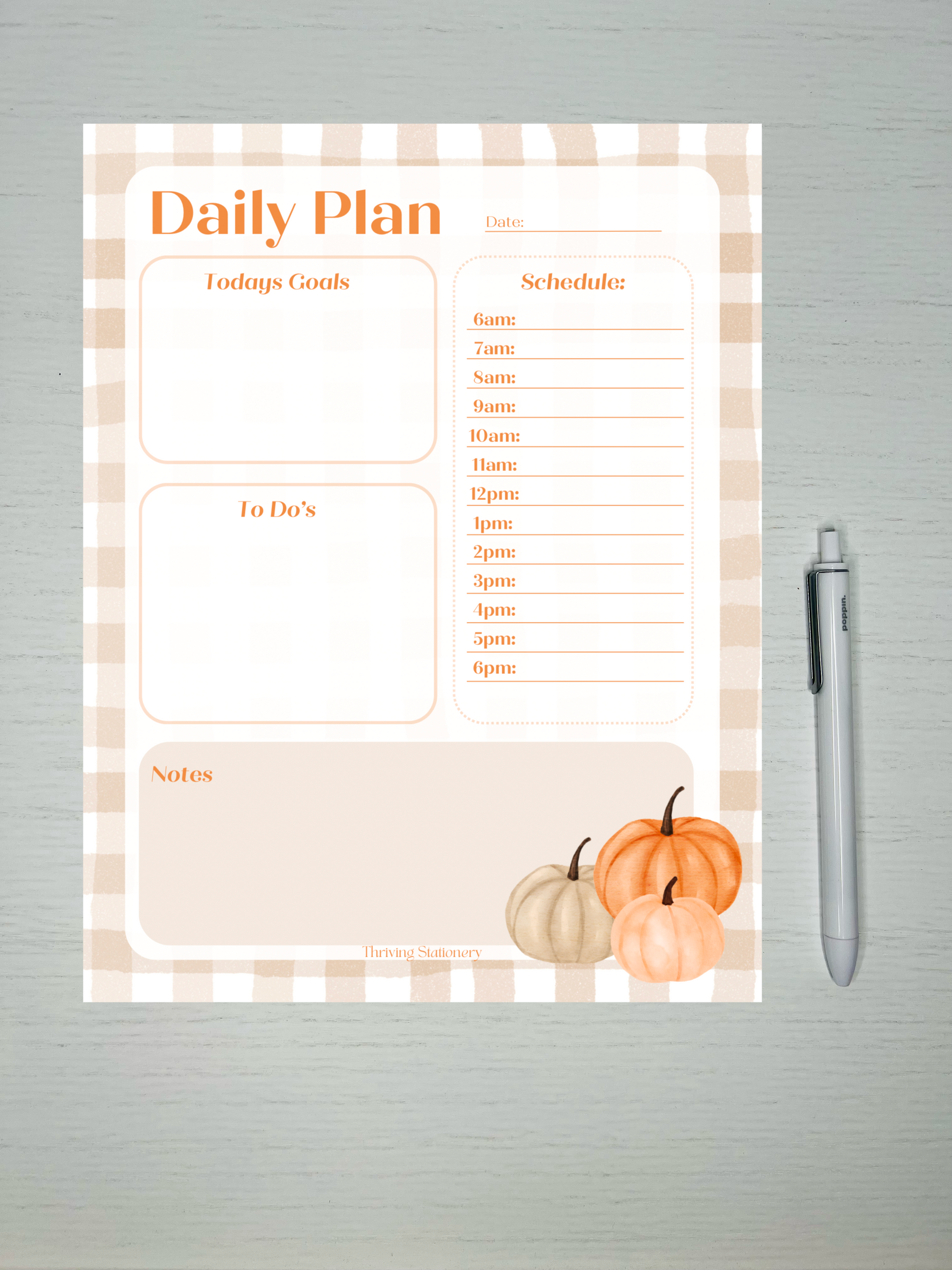 A Pumpkin Vibes Daily Planner with a pumpkin and leaves design, featuring sections for daily planning and schedules, accompanied by a pen.