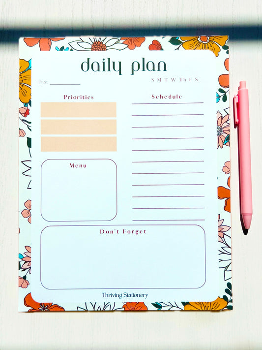 A planner pad with a floral design on the cover, labeled 'Daily Plan' with sections for personal information, schedule, menu, and notes.