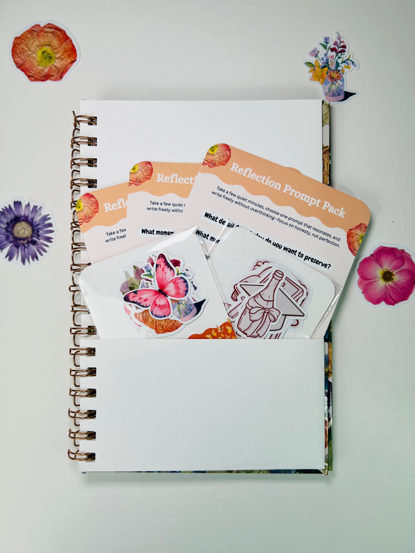 Notebook with reflection prompt cards and stickers on a white background with decorative flowers.