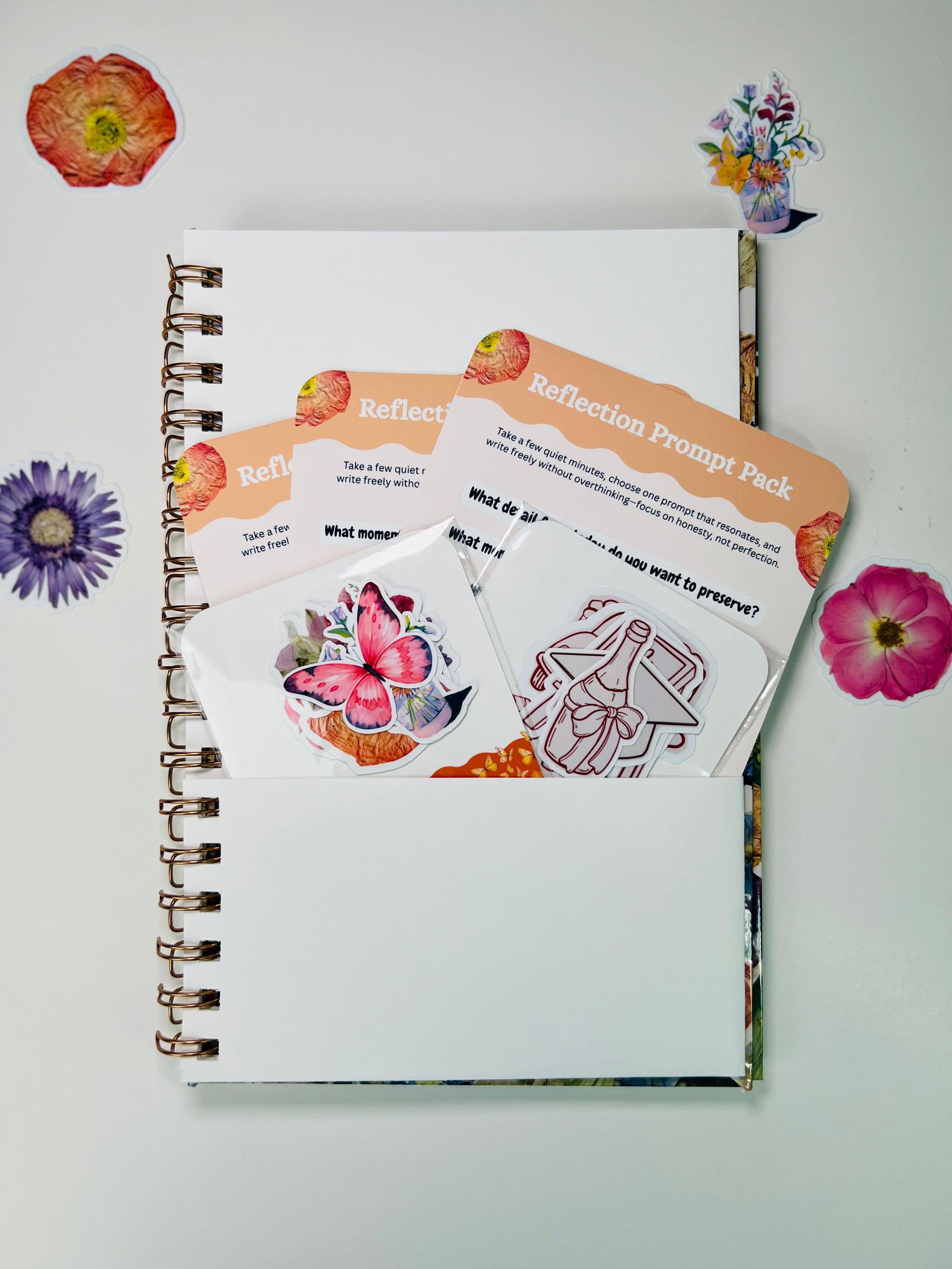 Notebook with reflection prompt cards and stickers on a white background with decorative flowers.