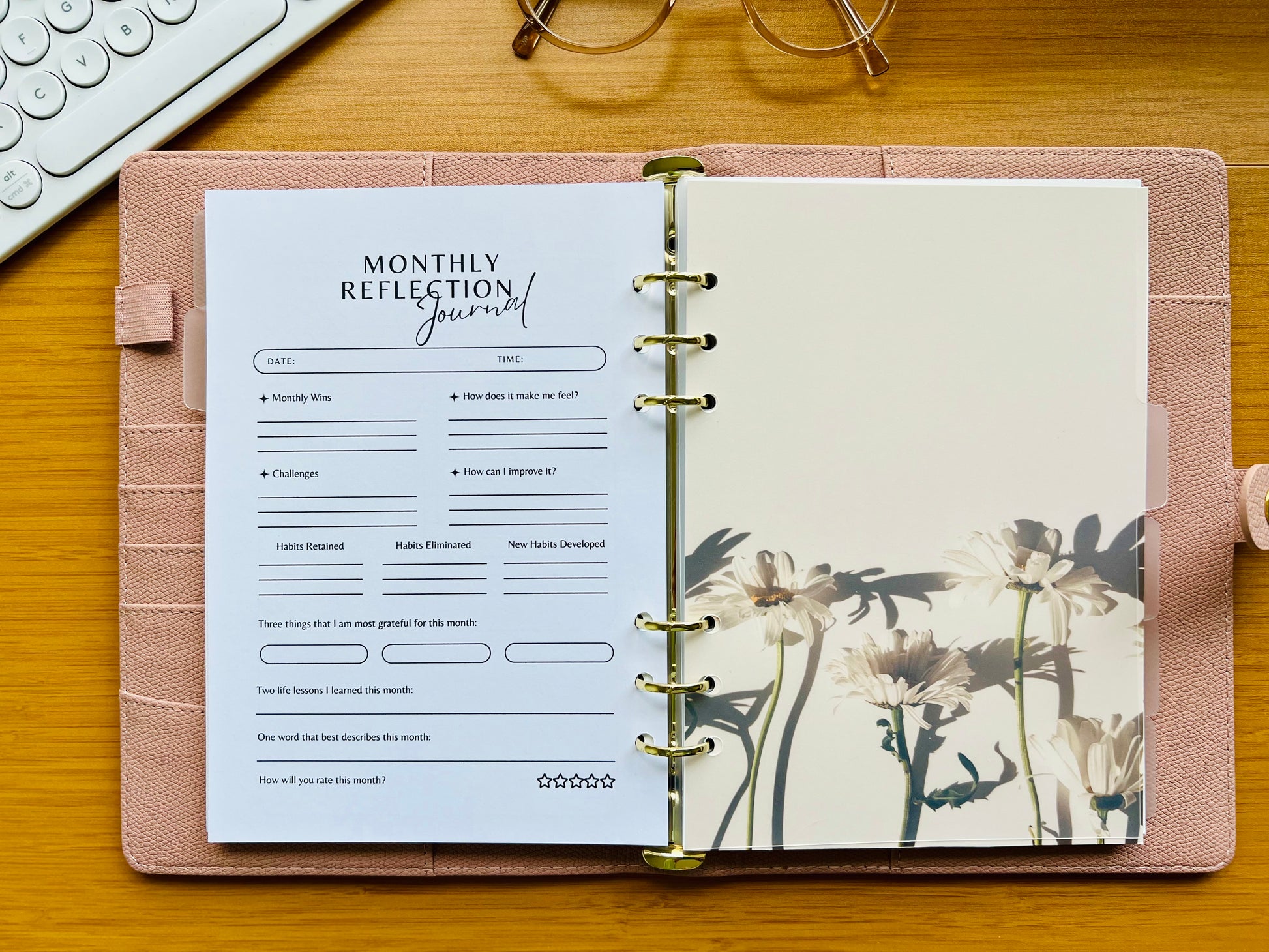 Monthly reflection journal in a pink planner on a wooden surface with a keyboard and glasses in the background.