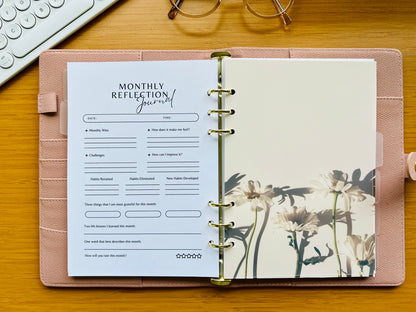 Monthly reflection journal in a pink planner on a wooden surface with a keyboard and glasses in the background.