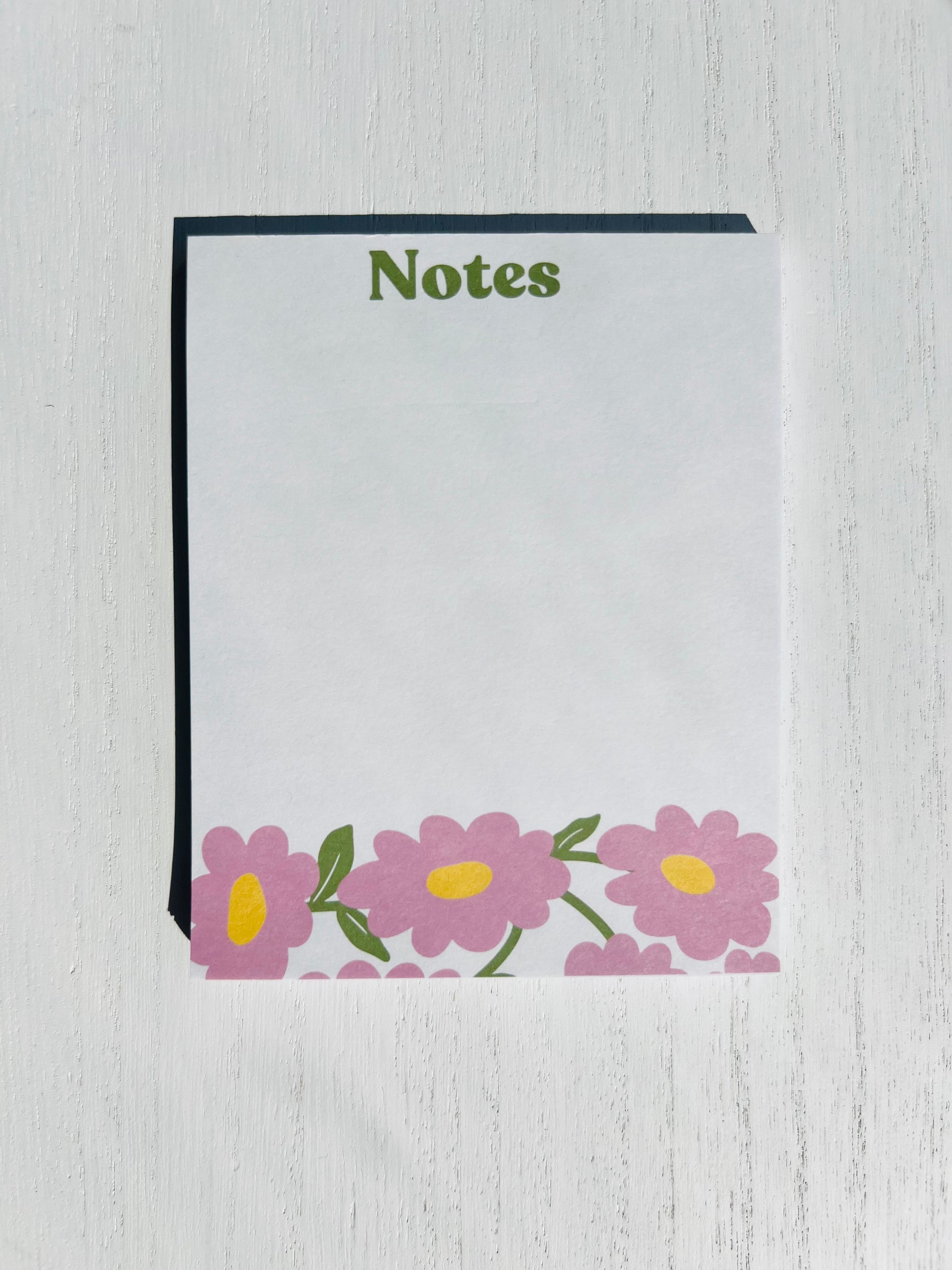 A notepad with a white cover and floral designs at the bottom, titled 'Notes' on the top.