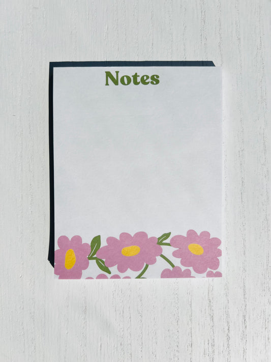 A notepad with a white cover and floral designs at the bottom, titled 'Notes' on the top.