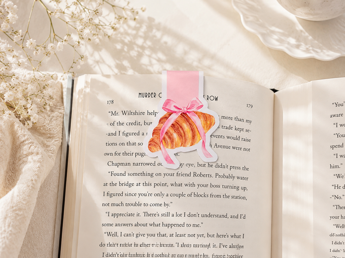 Open book with a croissant bookmark on a soft, light background