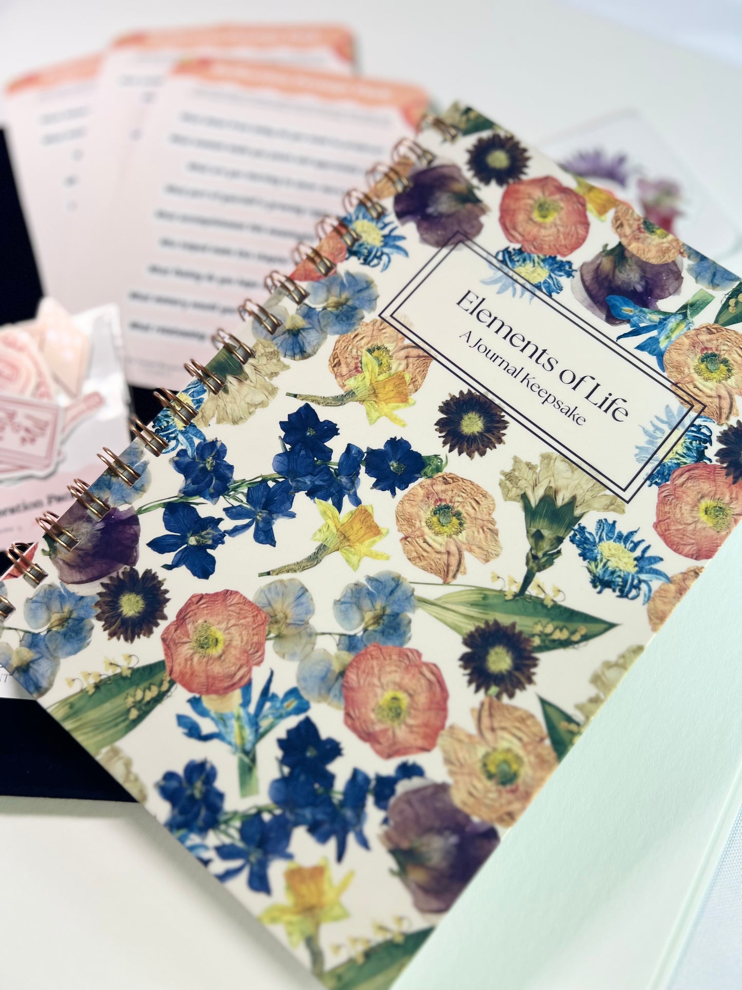 Floral patterned notebook with 'Elements of Life' title on a white surface