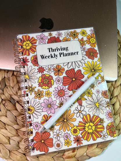 Floral planner with 'Thriving Weekly Planner' text on a woven surface