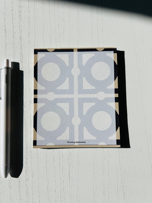 Square notepad with a bold geometric tile pattern in soft gray and cream tones. Black accents add a modern contrast. “Thriving Stationery” branding appears at the bottom.