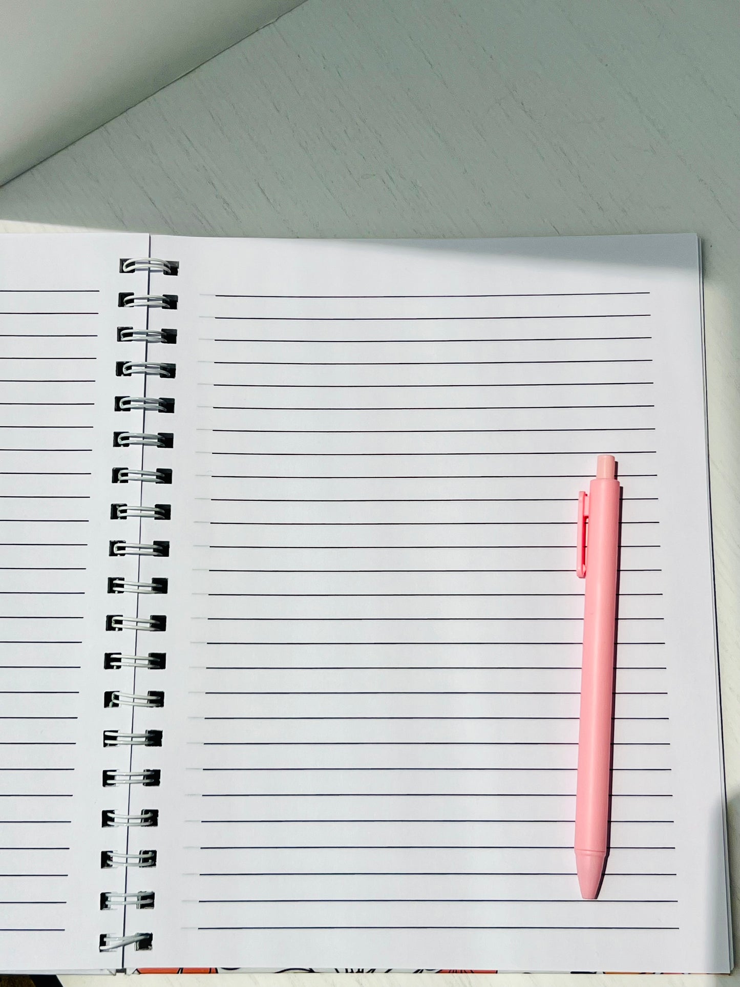 Blue Floral Spiral Notebook with white cover and navy floral pattern, lined pages, with a pen for scale