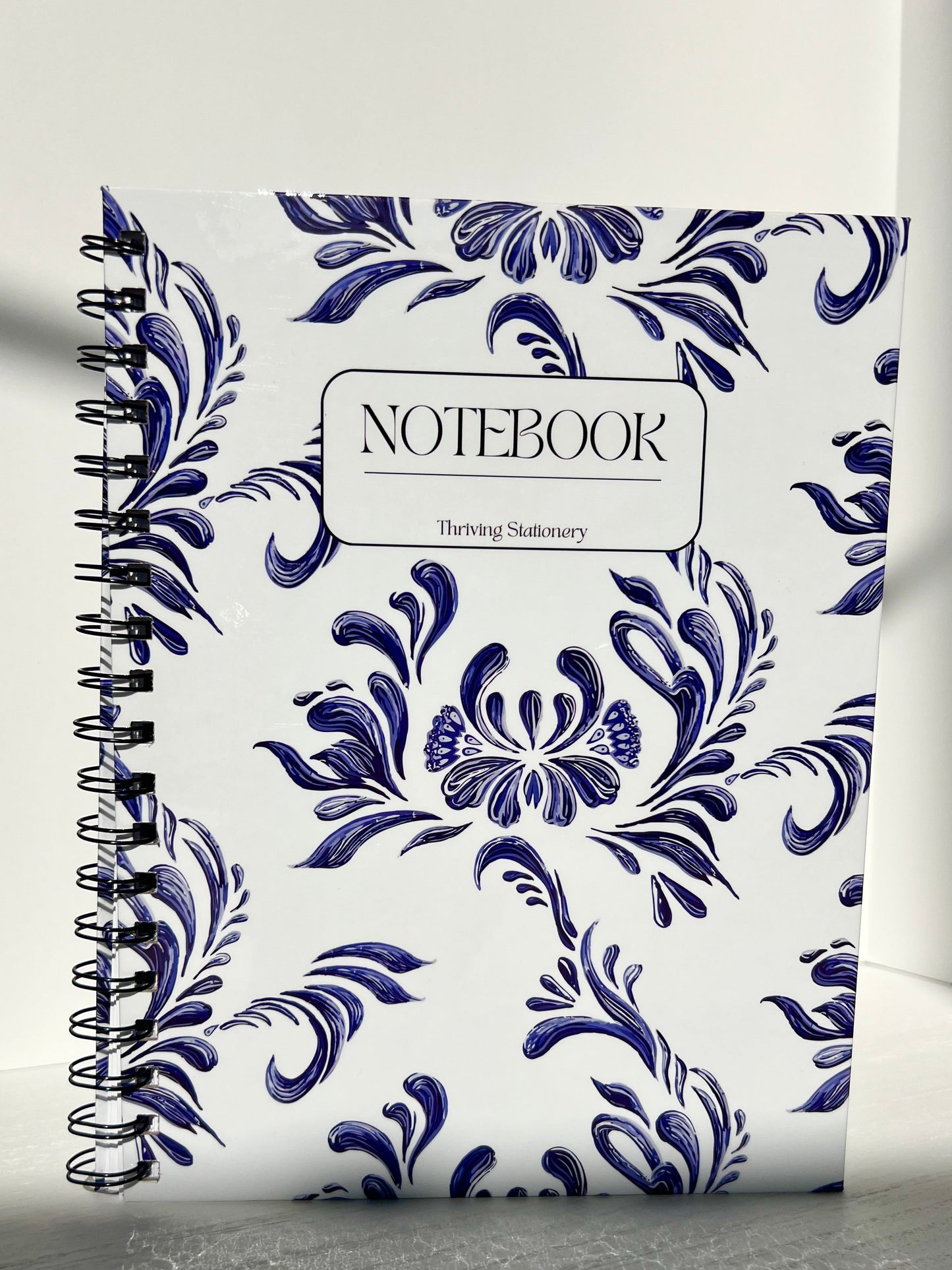 Aesthetic blue and white spiral notebook with floral design, hardcover finish, and “Notebook” label by Thriving Stationery.