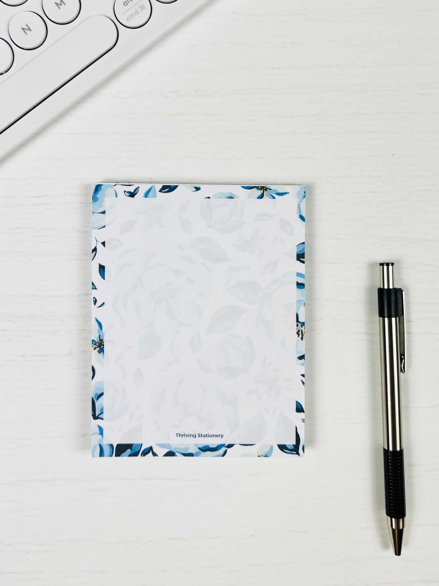 Small notepad with floral design on a white surface next to a pen