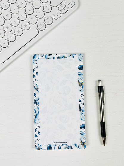 Notepad with floral design next to a pen and keyboard on a white surface