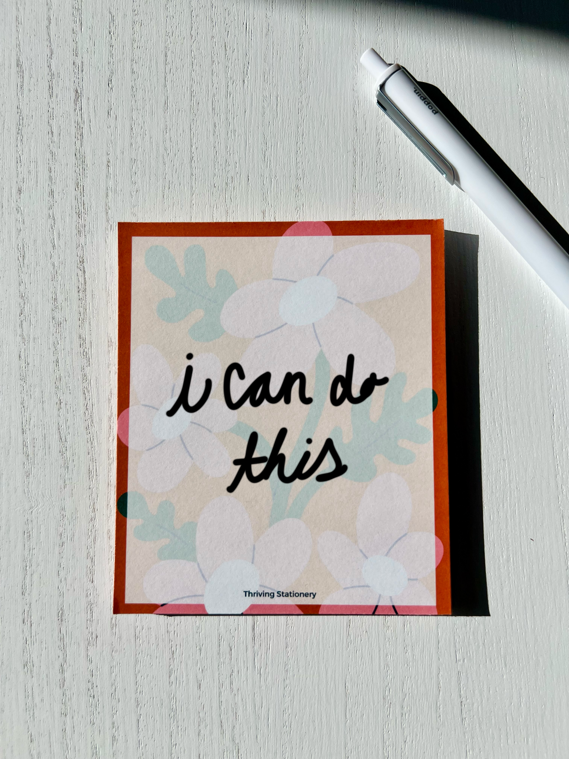 Colorful floral notepad with large, playful blooms in soft pastels and a bold orange border. “Thriving Stationery” logo at the bottom center.
