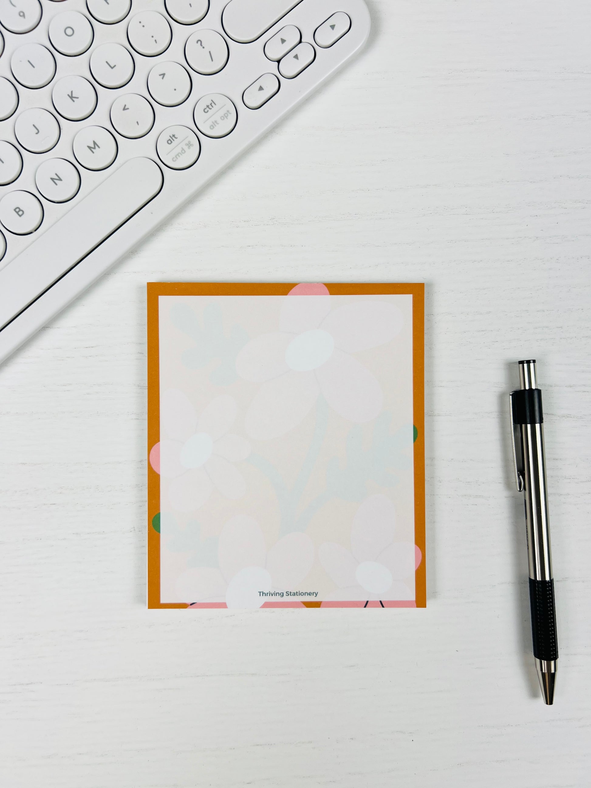 Notebook with floral border on a desk with a keyboard and pen