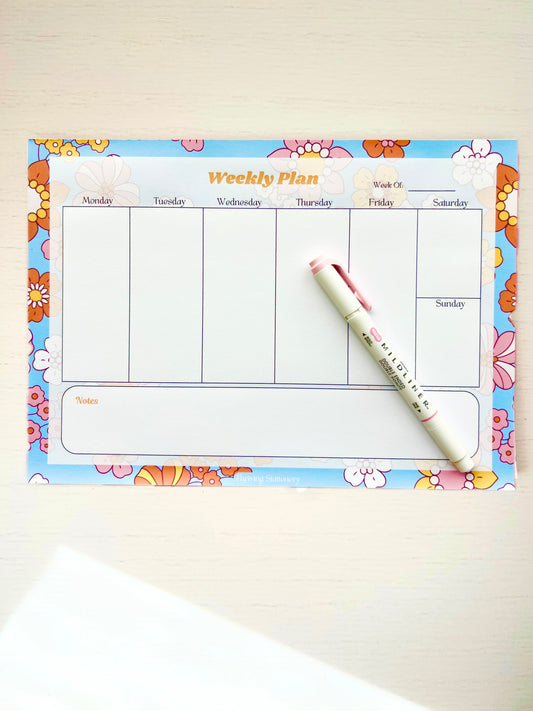 Colorful floral-themed weekly planner notepad with 7 columns for each day of the week and a large notes section at the bottom.