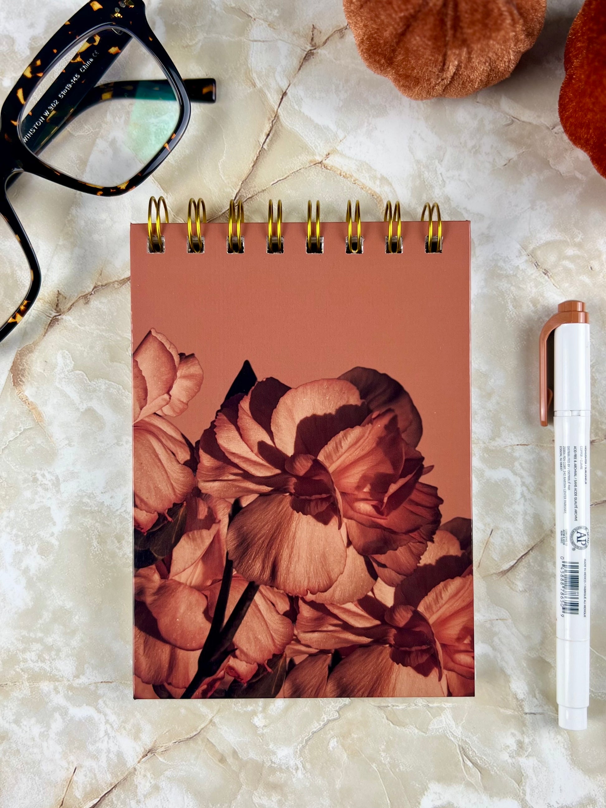 Notebook with floral design on a marble surface with glasses and markers.
