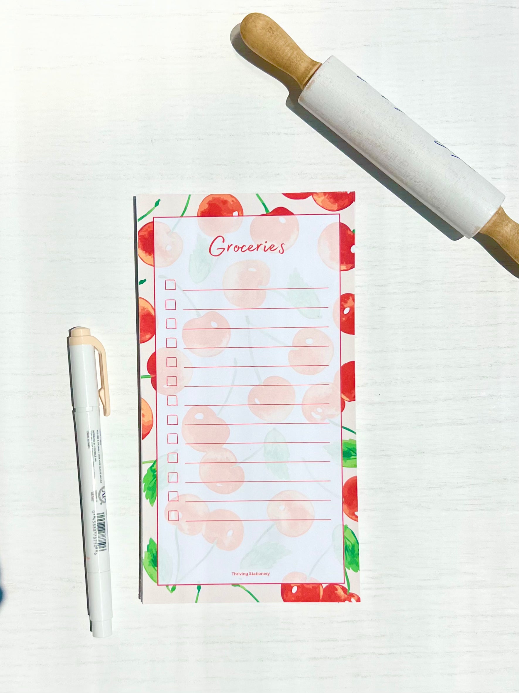 Cherry Grove Magnetic Grocery List Notepad with red cherry illustrations and lined layout with a pen for scale