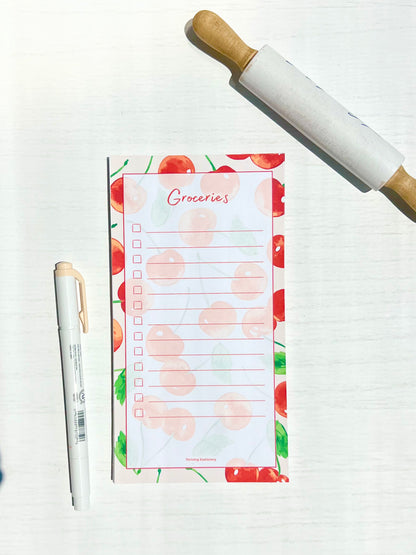 Cherry Grove Magnetic Grocery List Notepad with red cherry illustrations and lined layout with a pen for scale