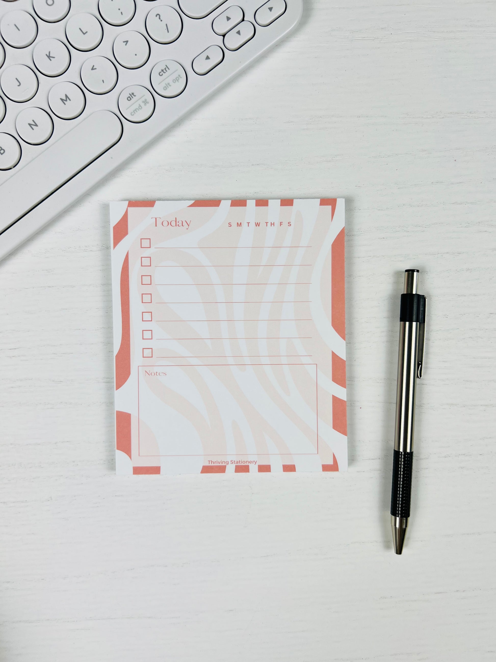 Coral Flow Daily Planner Notepad with coral and cream wavy border, checklist, and notes section with pen for scale