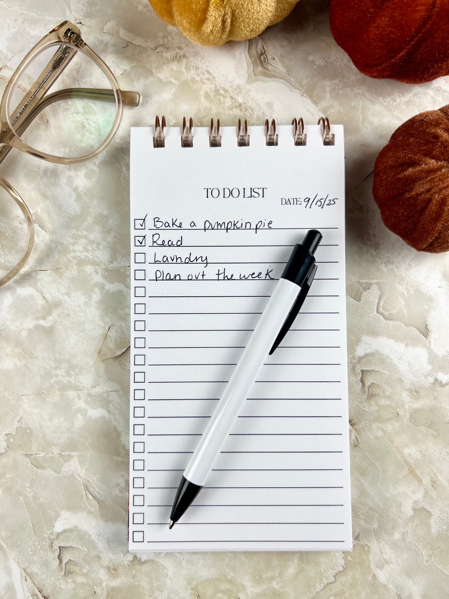 Notepad with a to-do list on a marble surface with pumpkins and glasses.