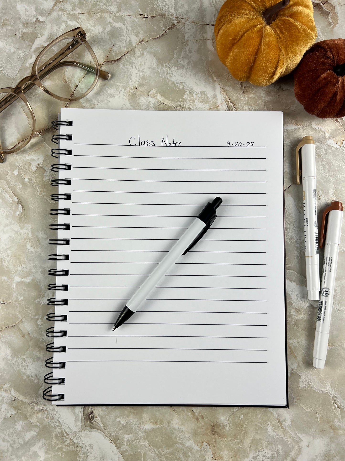 Notebook with lined pages, pen, and glasses on a marble surface
