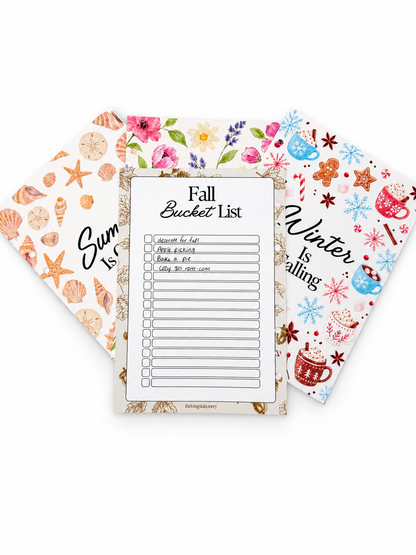 Three decorative planner or journaling pages fanned out on a white background: a central 'Fall Bucket List' sheet, a left 'Summer Bucket List' sheet with beach motifs, and a right 'Winter Bucket List' sheet with seasonal illustrations.