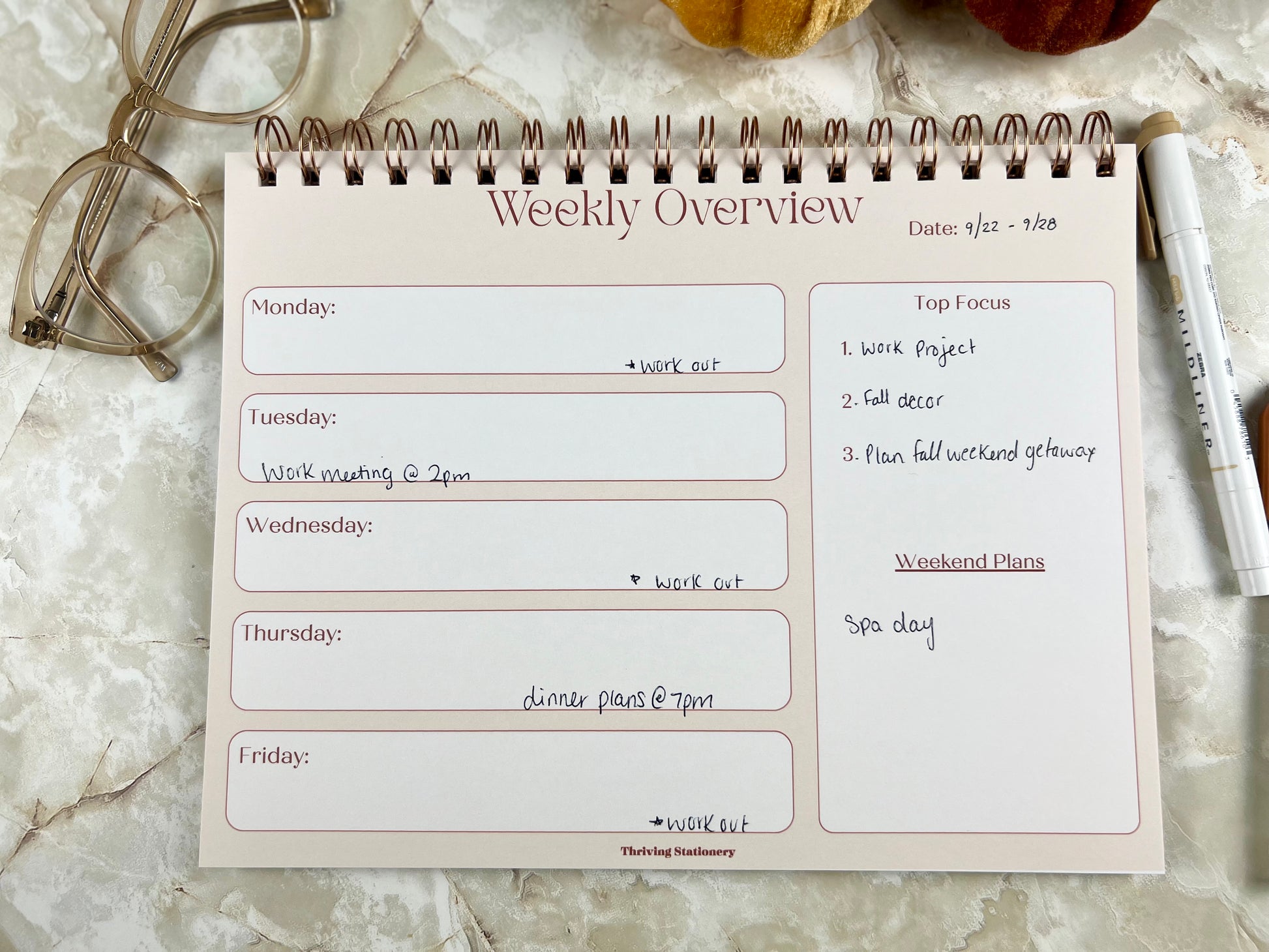 Weekly overview planner notepad on a marble surface with glasses and pen.
