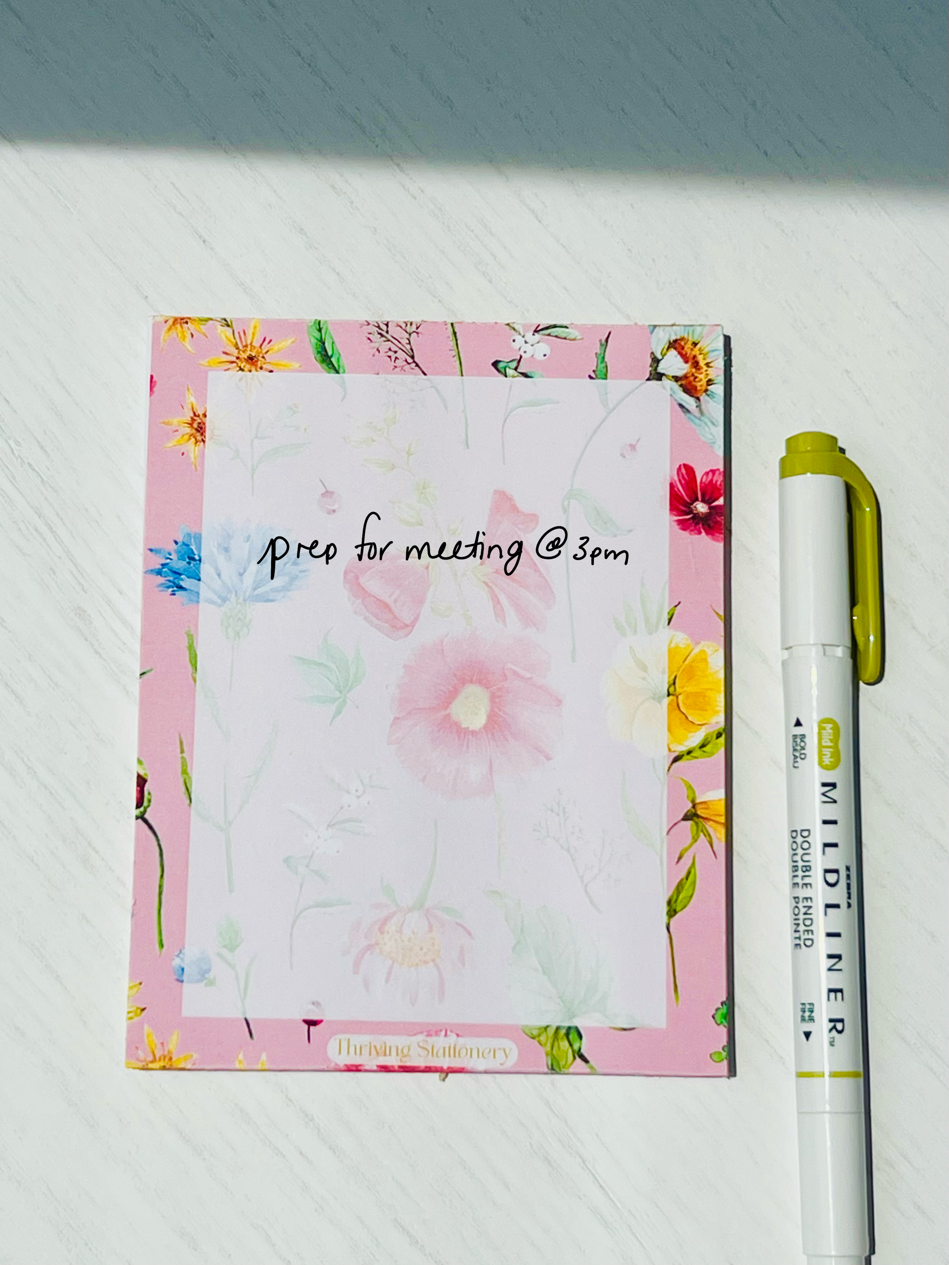 Floral notepad with soft watercolor wildflowers on a blush pink background. “Thriving Stationery” logo at the bottom center.
