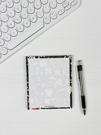 Notepad with floral border and pen on a white surface next to a keyboard