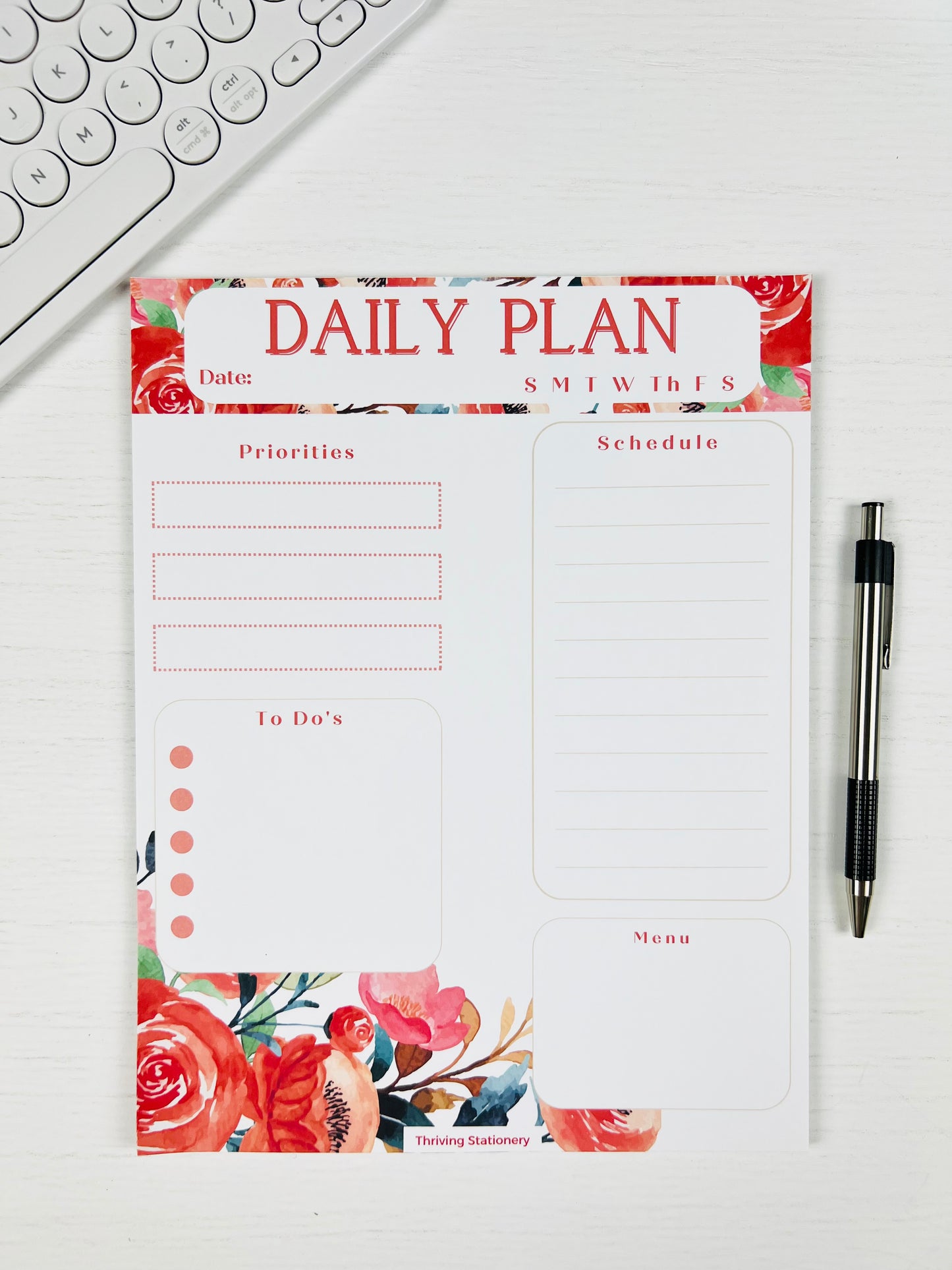 Daily plan notepad with floral design on a white surface with a keyboard and pen.