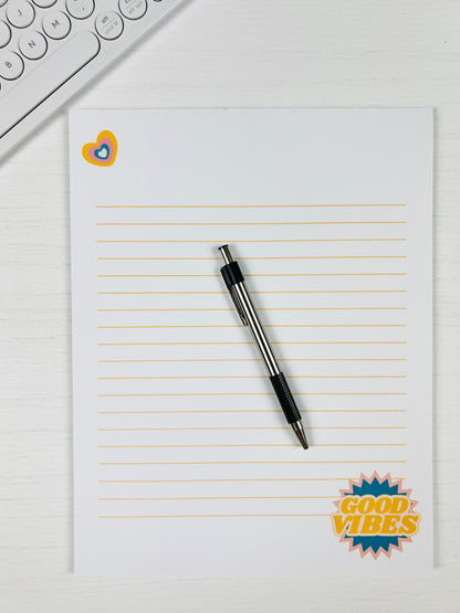 Good Vibes Large Lined Notepad with colorful text design and lined pages with a pen and keyboard for scale