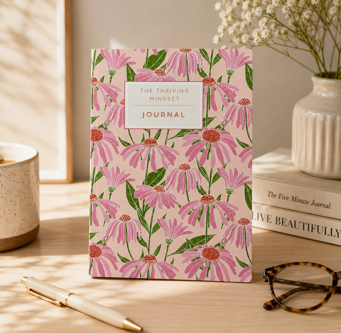 Journal with pink floral design on a wooden surface with a pen and glasses.