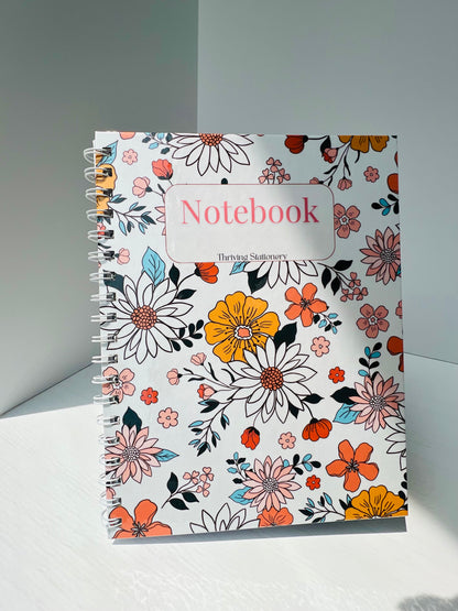 A floral garden lined notebook with a multicolor cover featuring various flowers and the text 'Notebook' on the front cover.