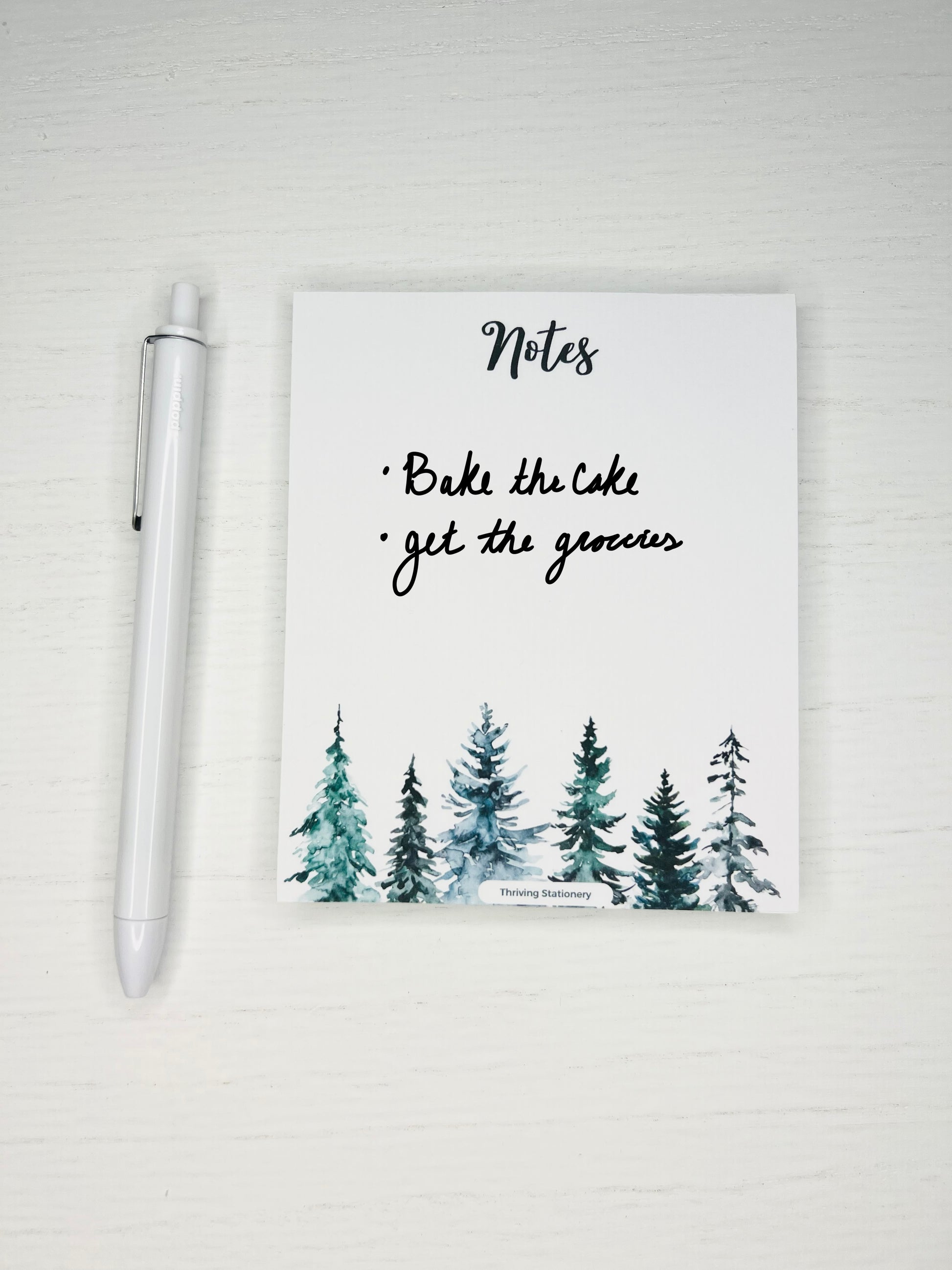 notepad with "Notes" in script at the top and watercolor pine trees across the bottom border.