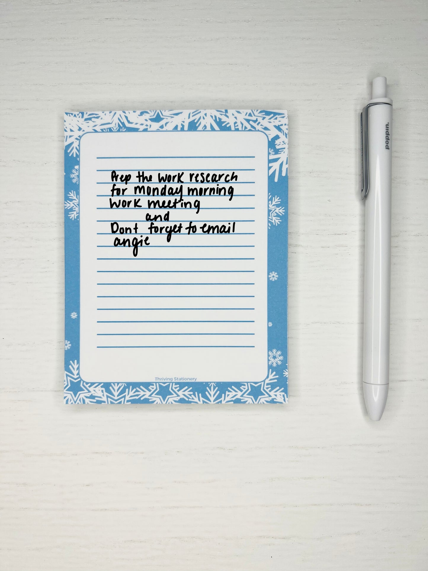 Blue winter-themed notepad with white snowflakes along the border and lined space in the center for writing.