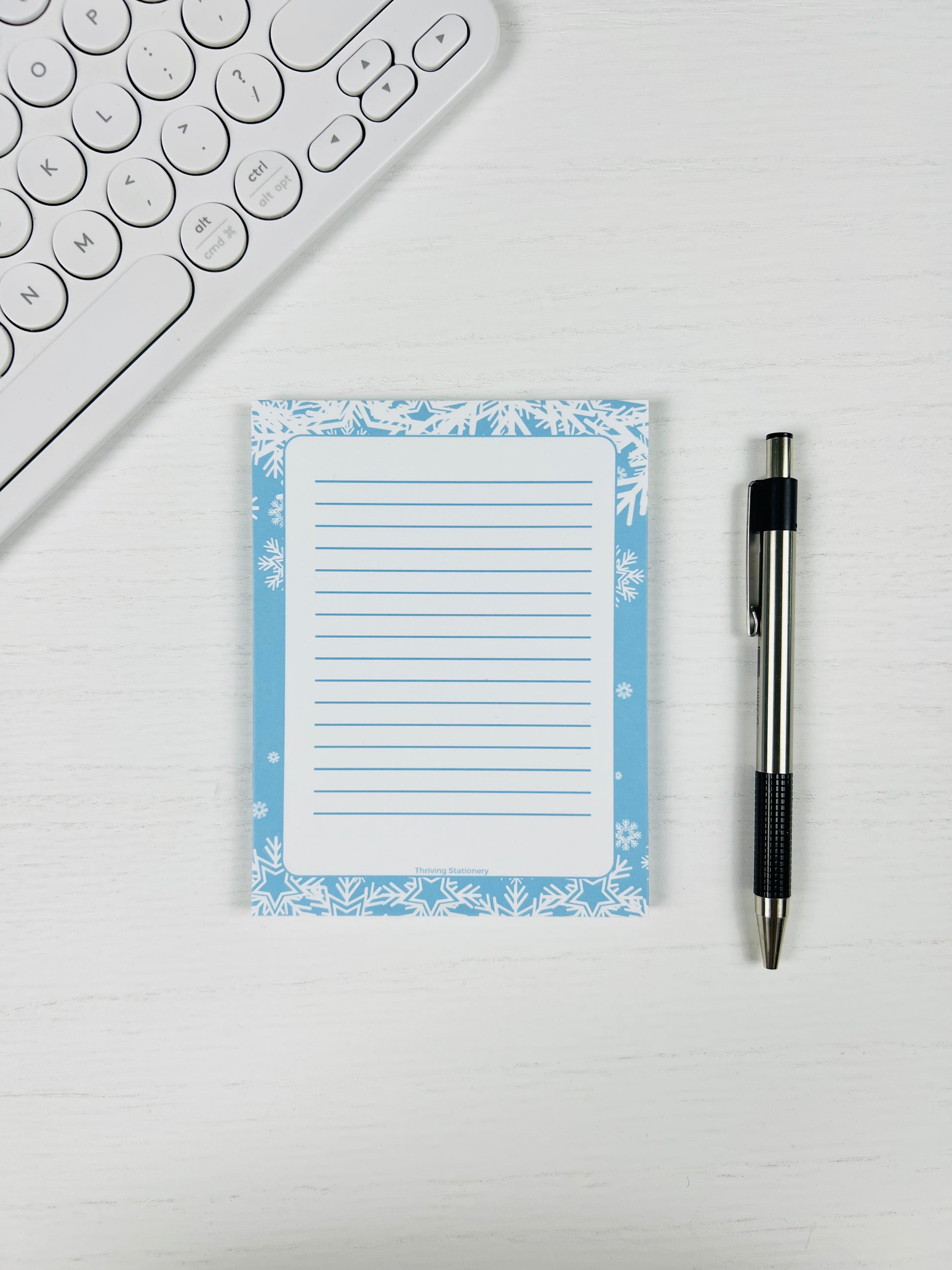 Notepad with floral border and pen on a white surface next to a keyboard