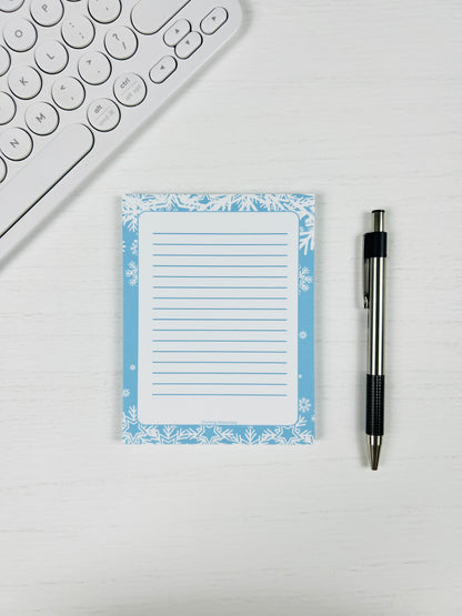 Notepad with floral border and pen on a white surface next to a keyboard