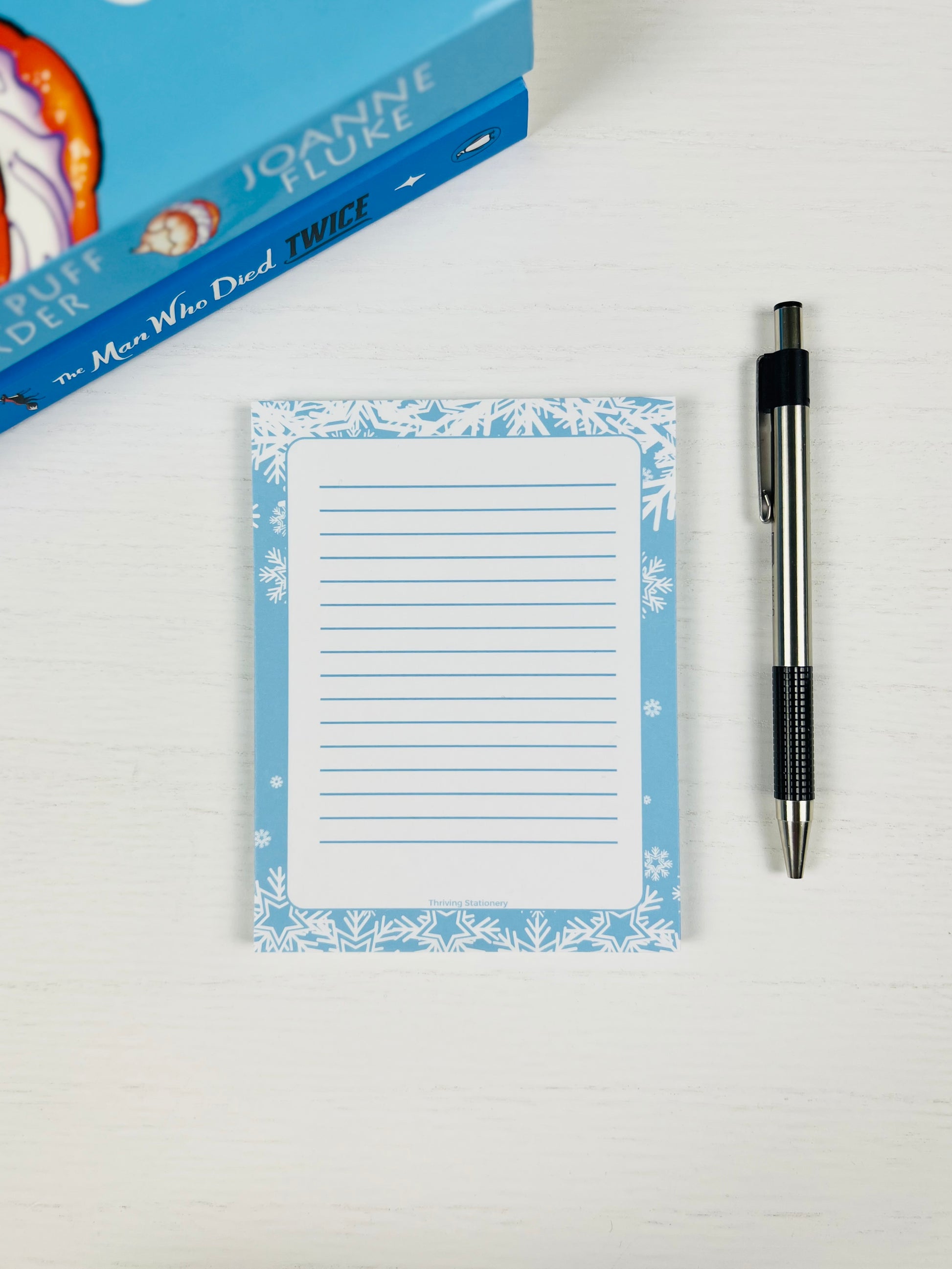 Notepad with floral border and pen on a white surface