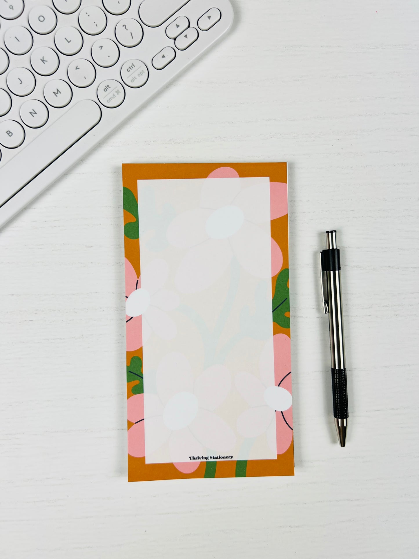 Floral notepad with a pen and keyboard on a white surface