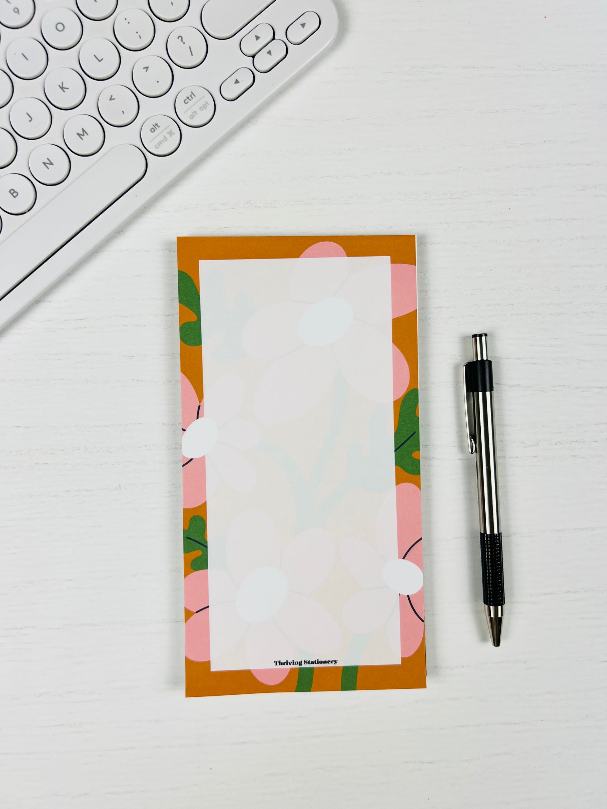 Floral notepad with a pen and keyboard on a white surface
